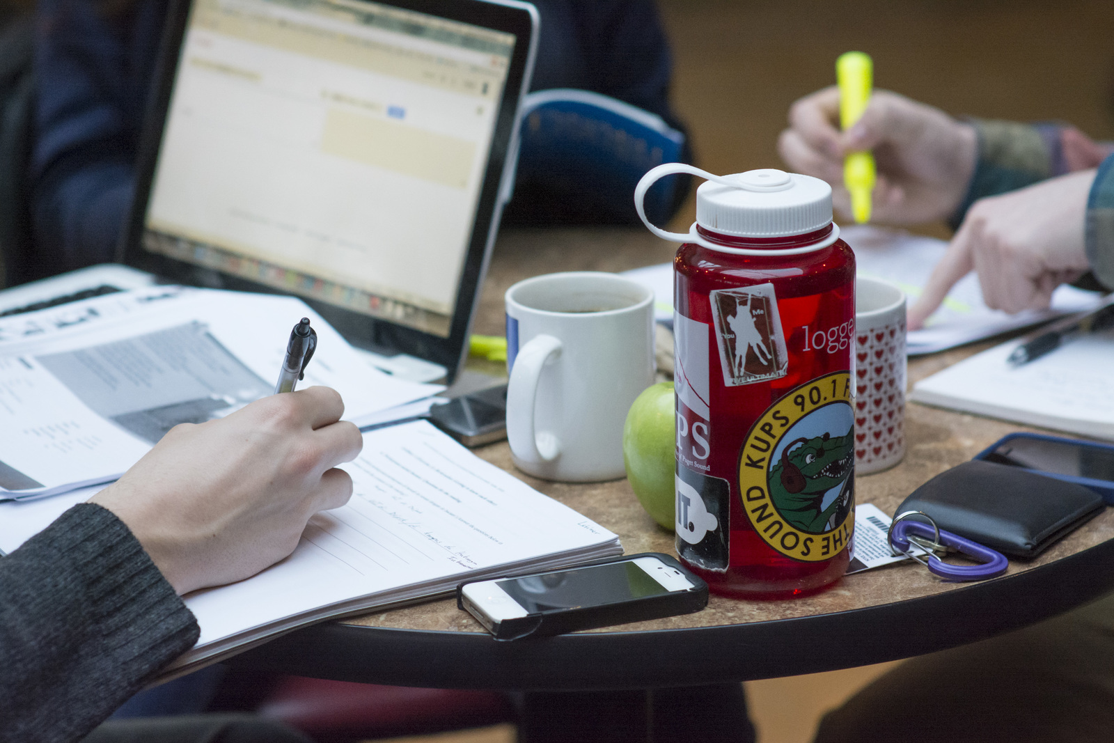 Student taking notes at a table with a laptop and water bottle