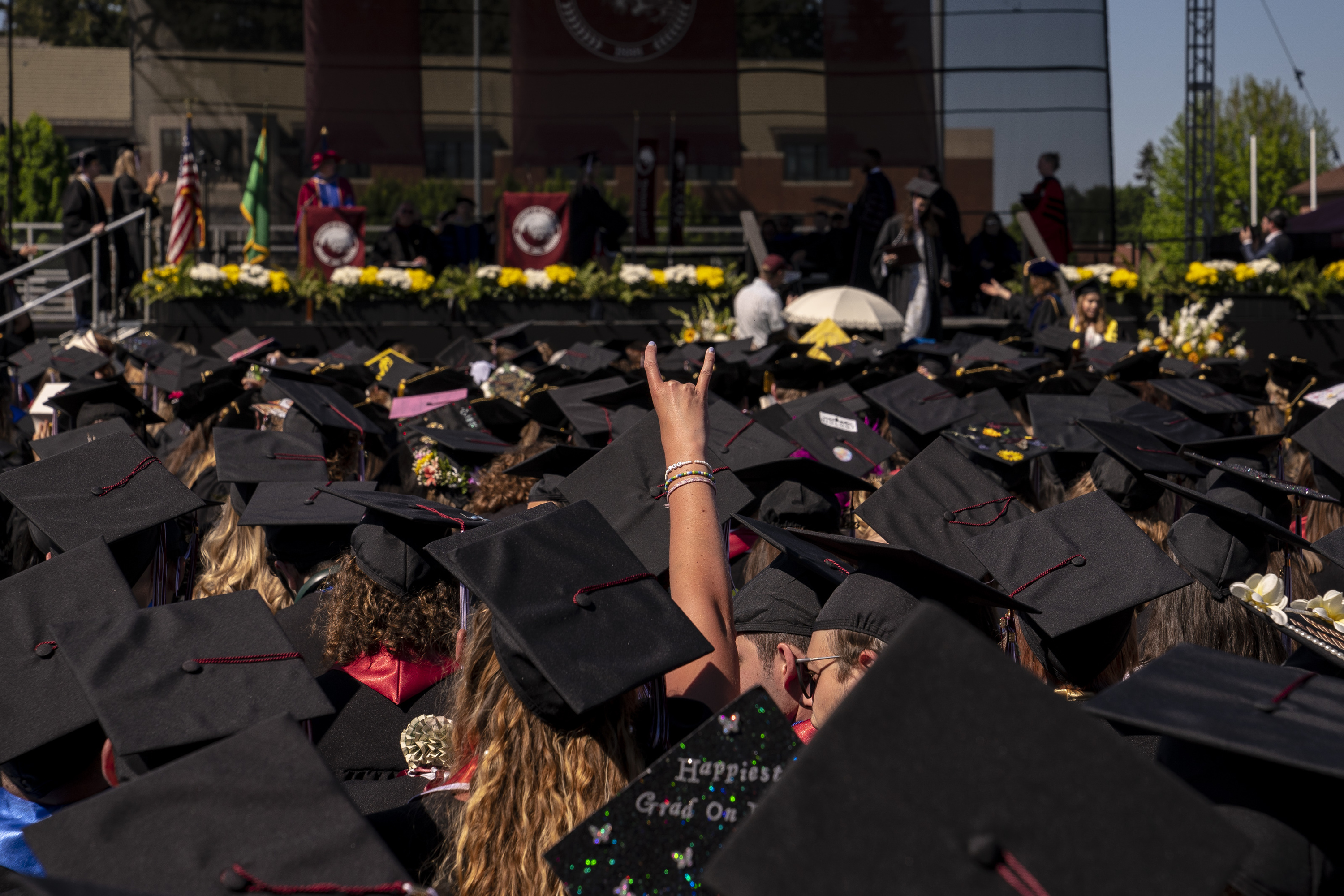 An arms shoots out above a dozen black mortar boards at a graduation ceremony. 