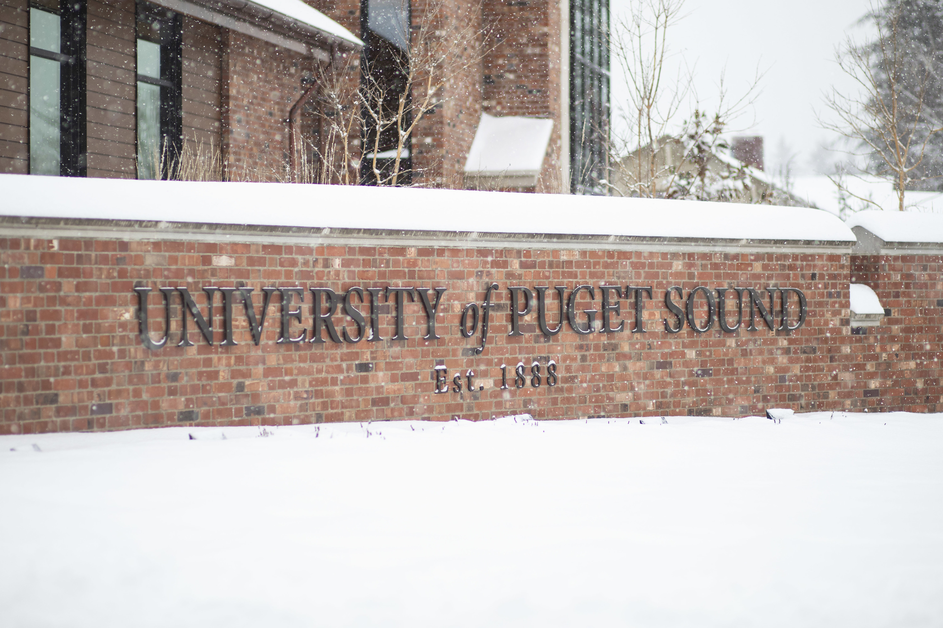 A brick University of Puget Sound sign sits covered in snow. 