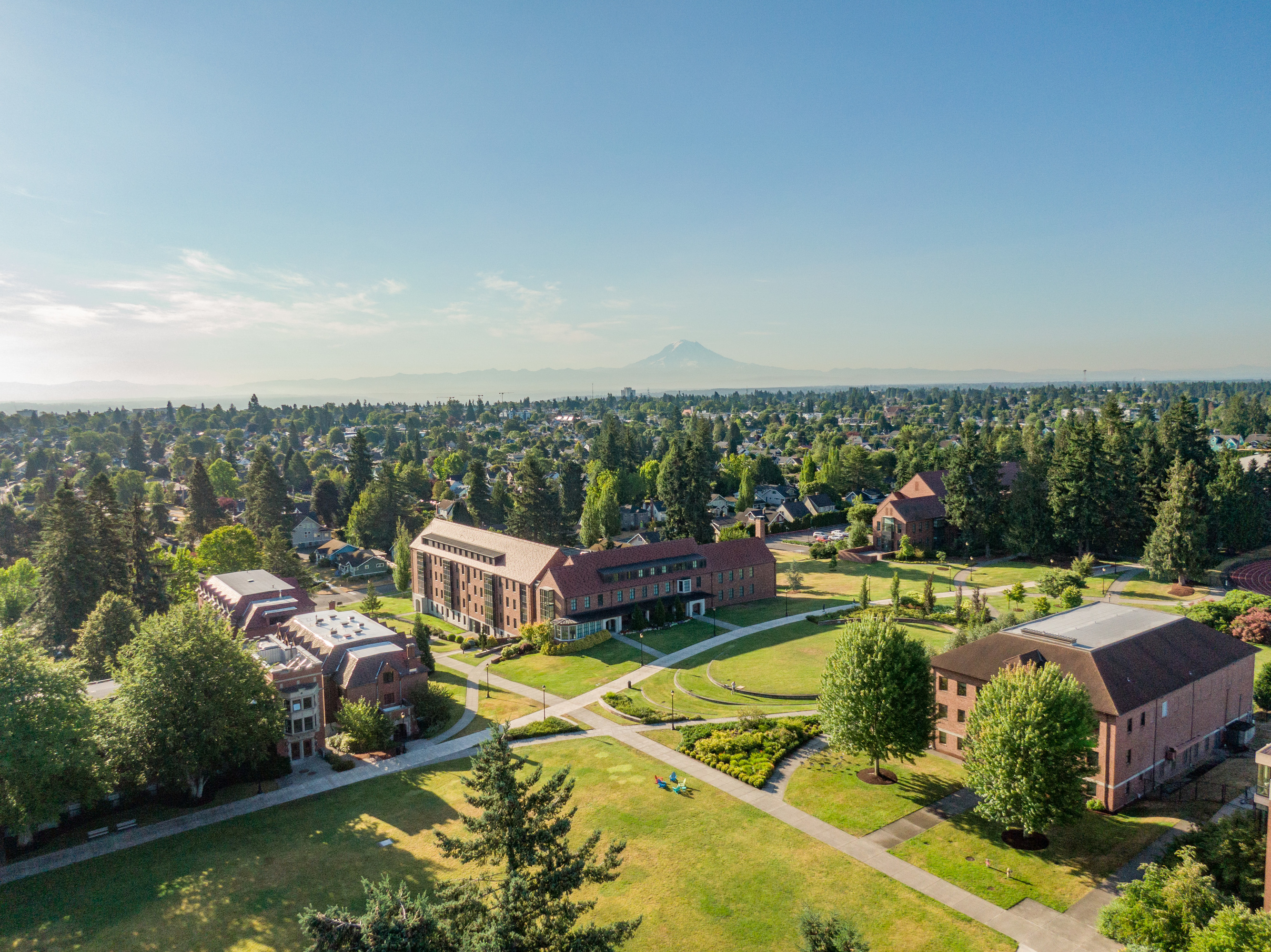 Image taken over campus with buildings below, trees stretched out to the horizon, and Mount Rainier in the distance.