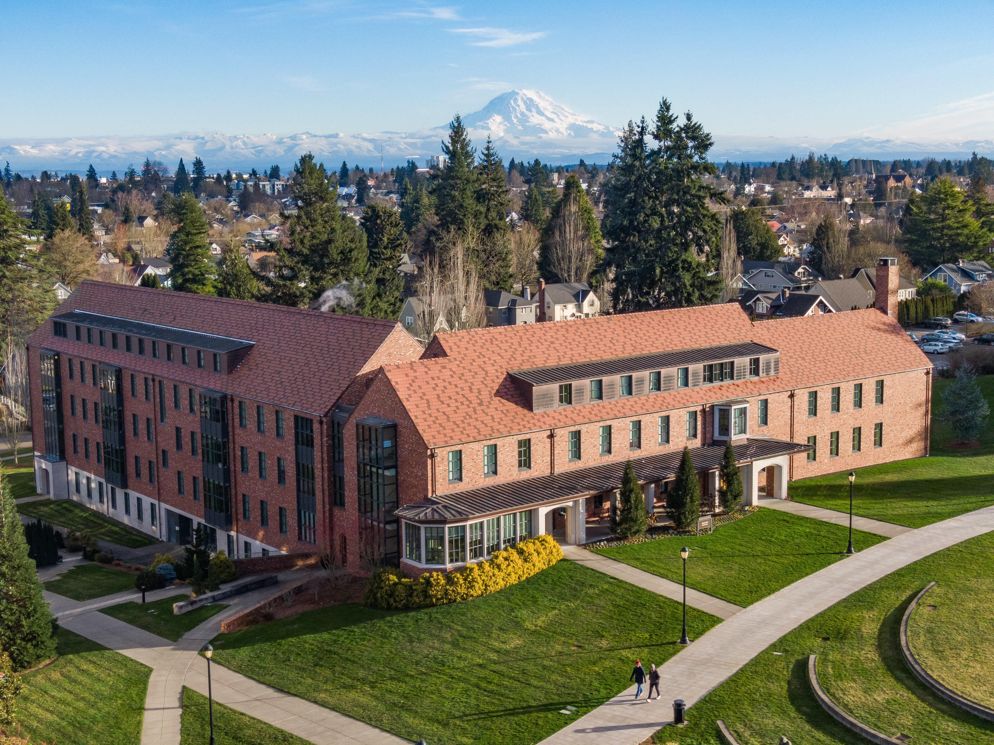 Aerial view of a red brick building with trees surrounding it and Mount Rainier in the background.