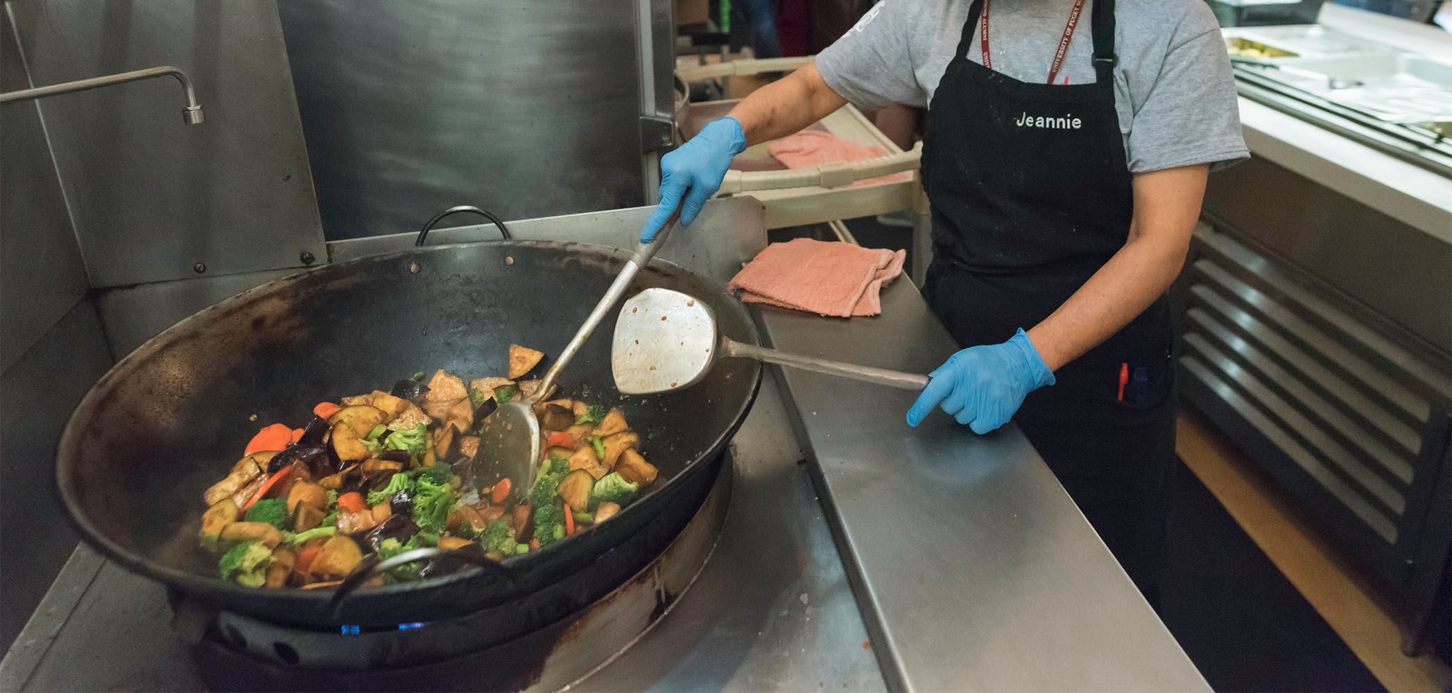 DES worker cooks food in a large wok.