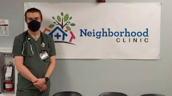 Ben Smith President of Phi Sigma standing in front of Neighborhood Clinic banner