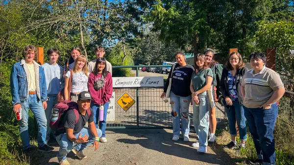 Students stand on a dirt road in front of a metal gate with a sign reading: Compass Rose Farms.