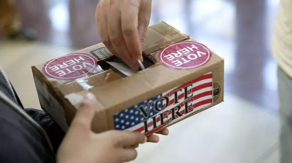 Person holding a ballot box while another person puts their vote into the box.