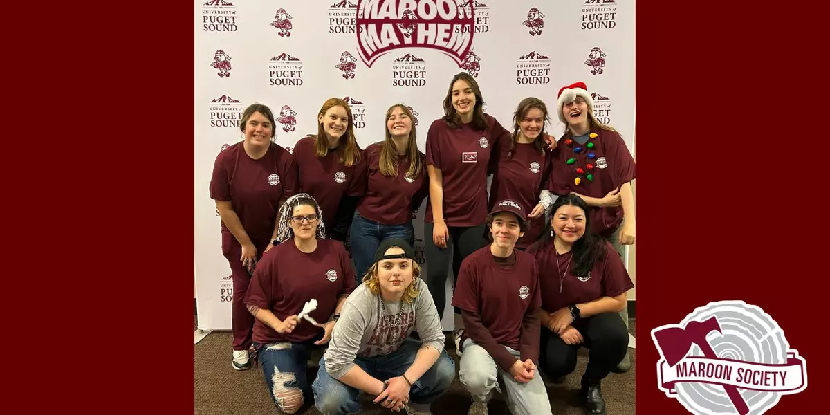 Group photo of Maroon Society members at a Maroon Mayhem event standing in front of a University of Puget Sound background