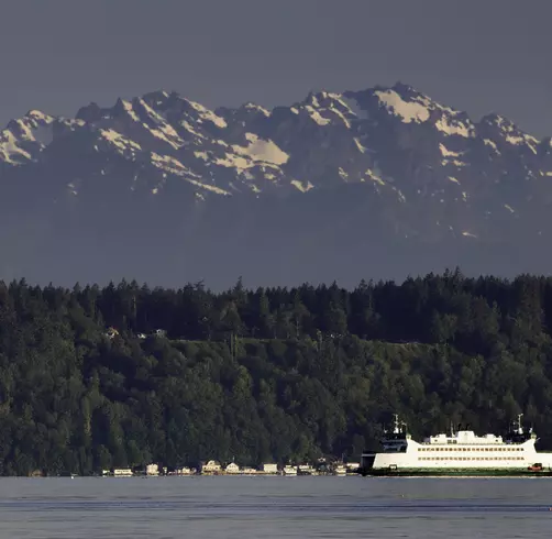 A Washington State ferry glides across the Puget Sound with one of the area's mountain ranges in the background.