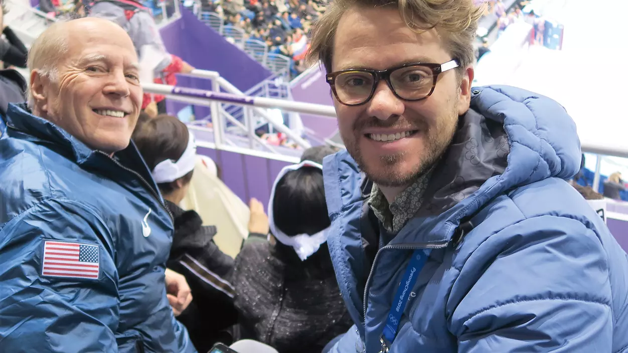 Two men in blue jackets seated in the audience of the Olympics