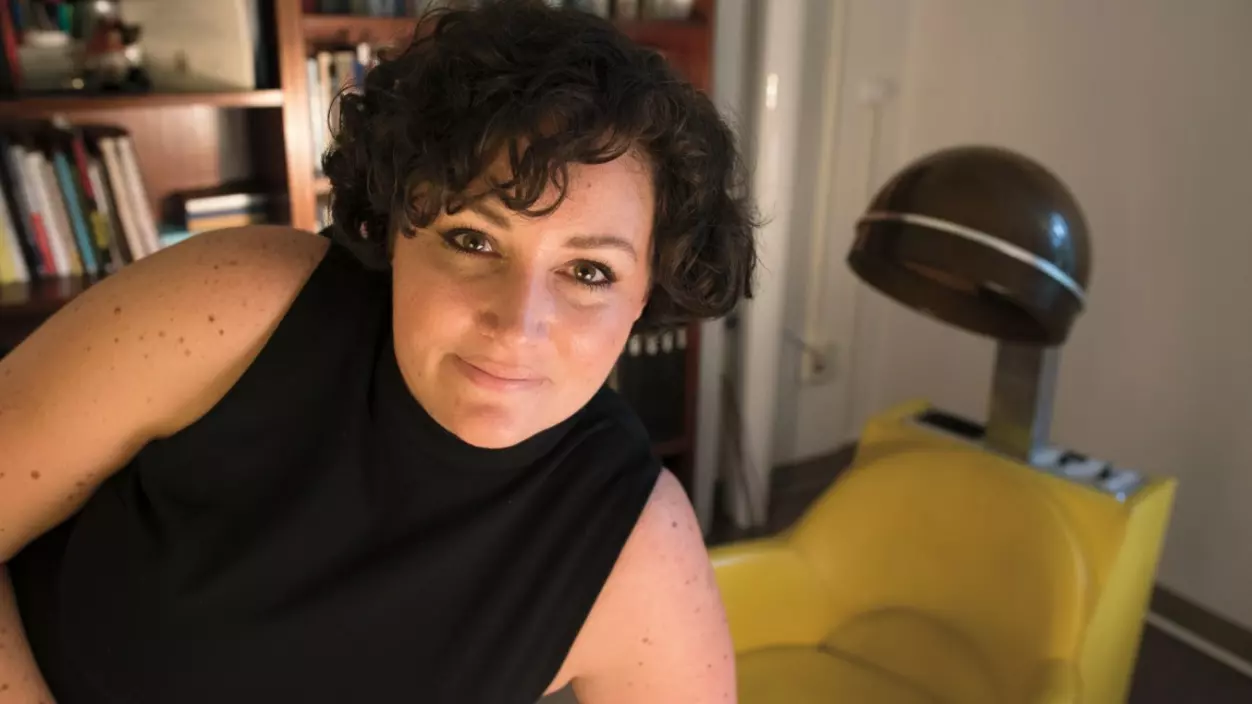 Person smiling in front of a bookcase and yellow chair