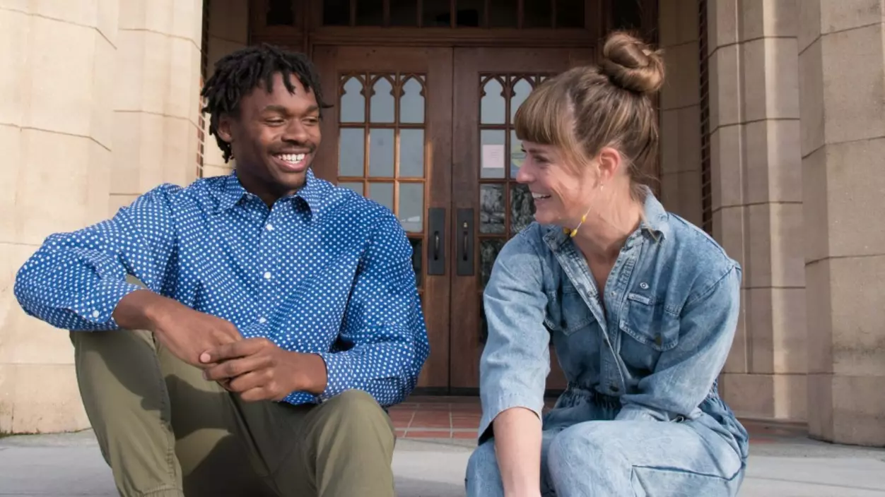 Two people smiling in front of the entrance of a school