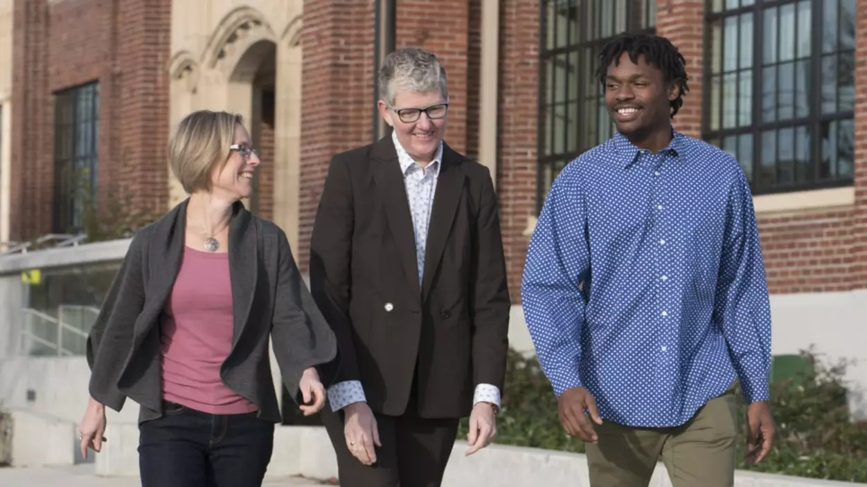 Three people walking in front of a school