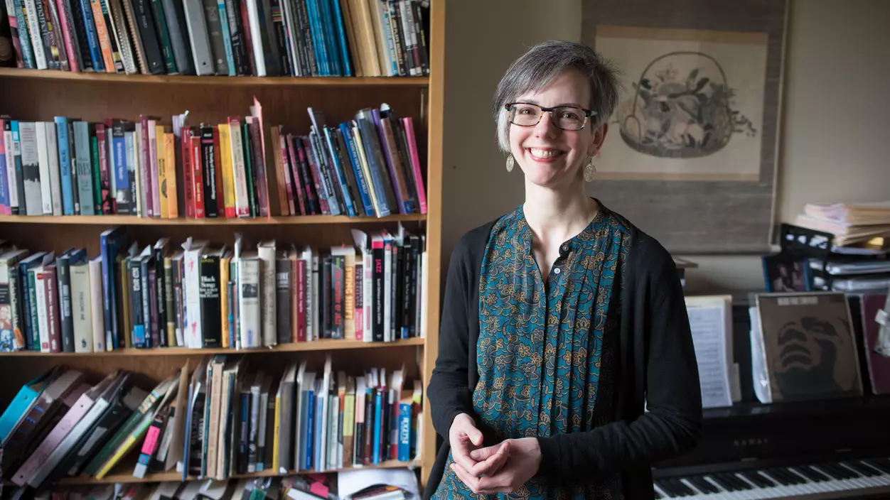 Person smiling in front of a bookcase and piano