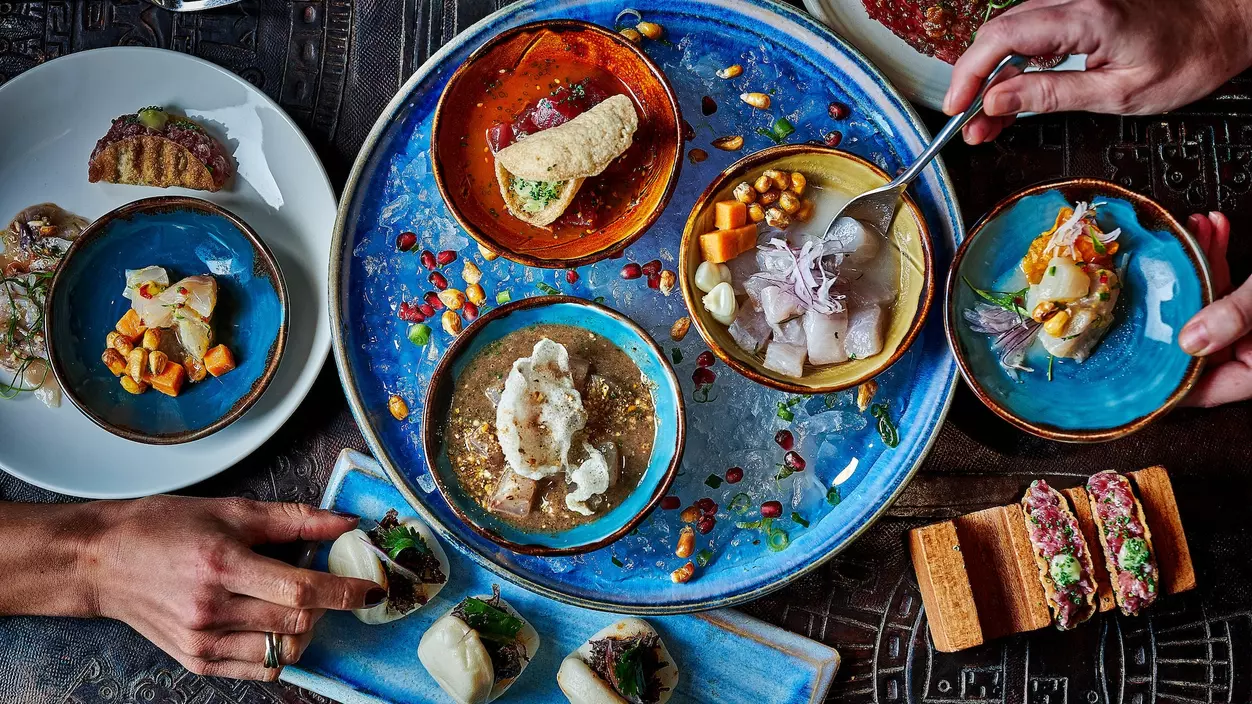 an overhead view of a table spread with food and hands reaching for colorful dishes.