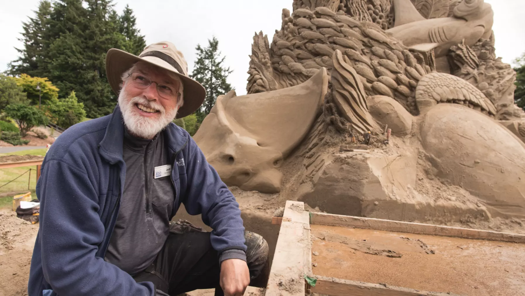 Jeff Strong smiling next to his sand sculpture and tools