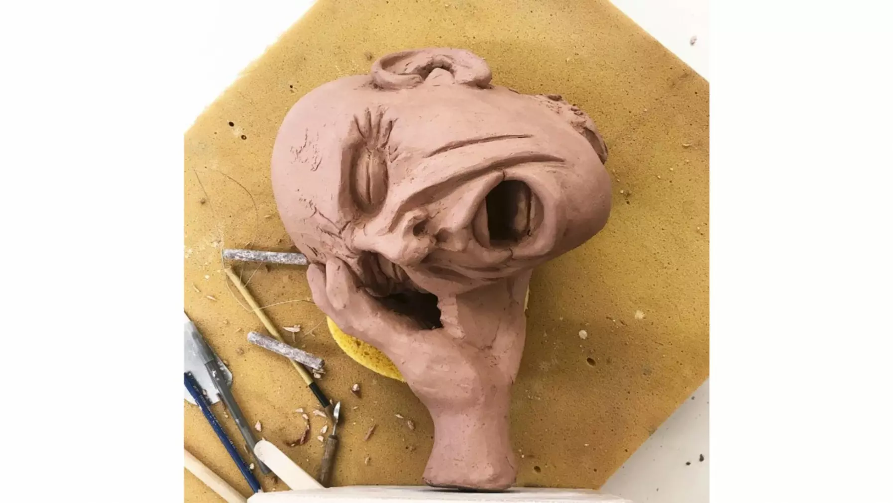 Clay sculpture of face with a hand on its right side in progress