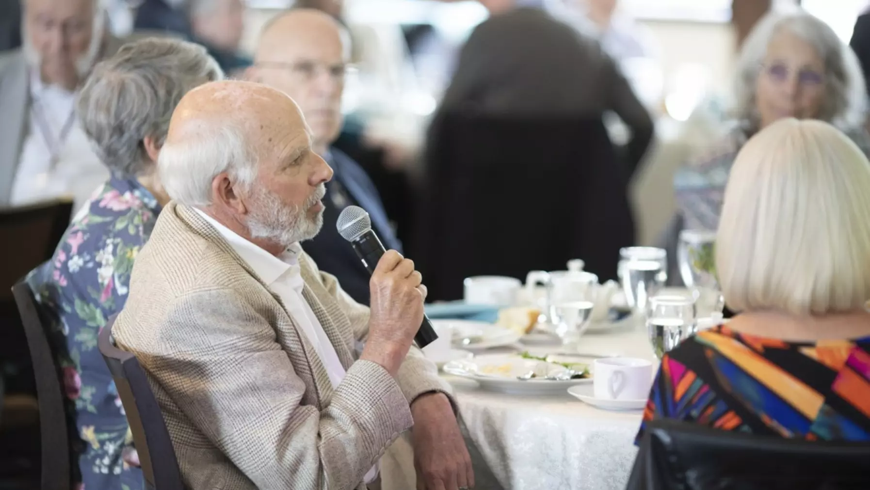 A person holding a microphone seated a table