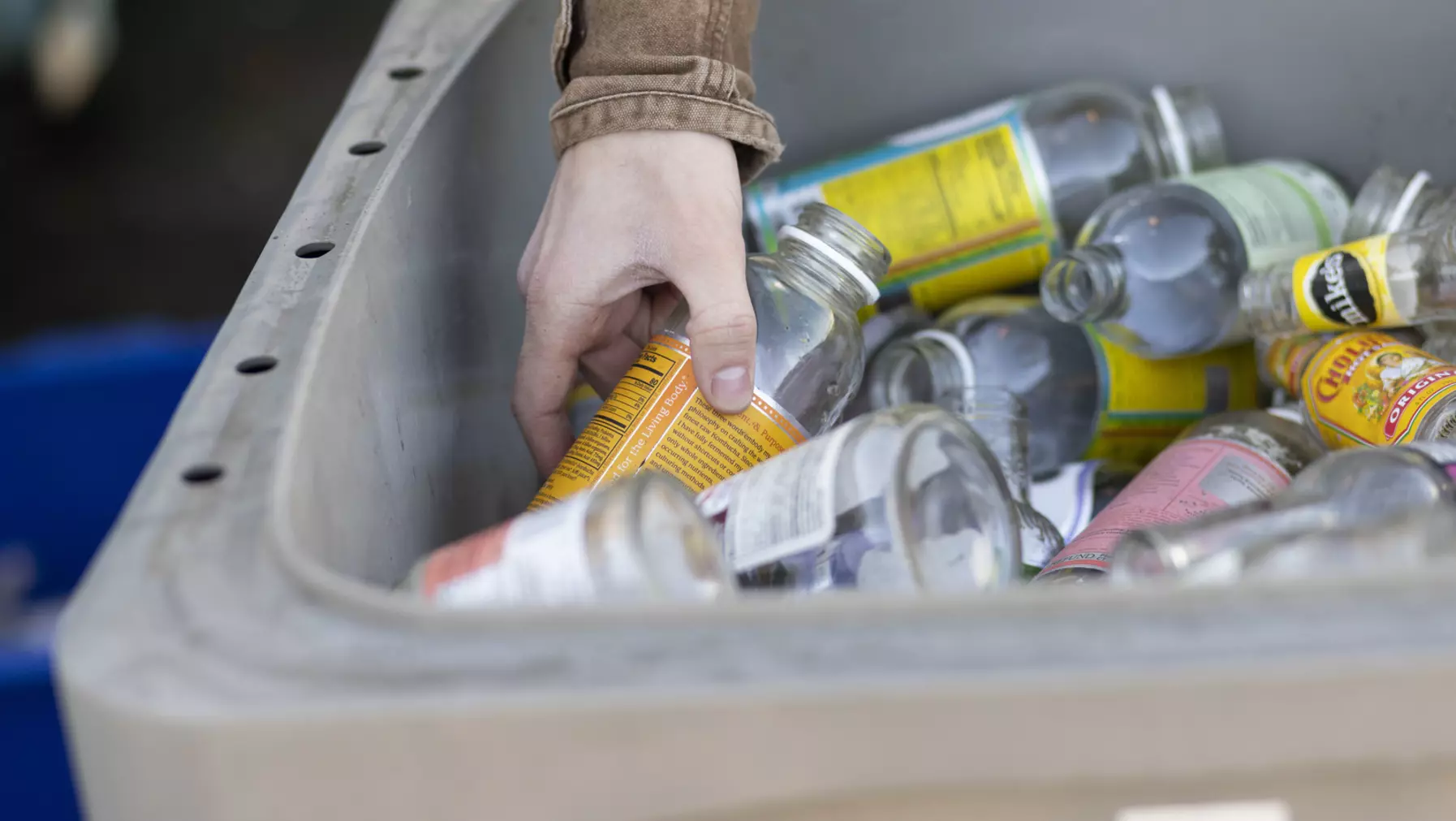 A hand reaches into a comingled recycling tote to pull a bottle out of the bin