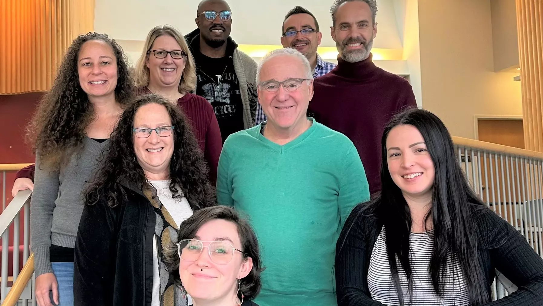 Psychology faculty and admin stand grouped together on the well lit stairs of Weyerhauser Hall, smiling