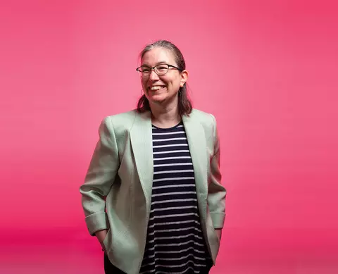 A person posing and smiling against a pink background